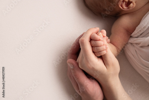 The hand of a sleeping newborn in the hand of mother and father close-up. Tiny fingers of a newborn. The family is holding hands. Studio macro photography. Concepts of family and love.