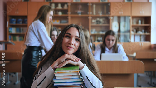 A student poses with textbooks at her desk in her class.