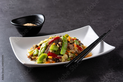 Beef, vegetables and sesame seeds inwhite plate on black background photo