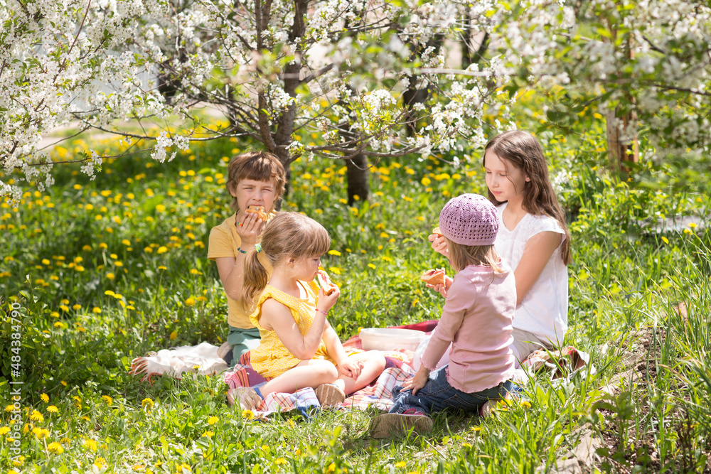 Fototapeta premium kids friends spend time together in nature. a group of children sit on the grass and having picnic in the spring garden