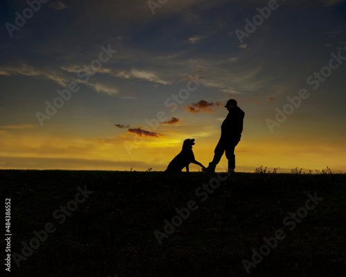 Sunset and silhouette of a man and his affectionate dog.