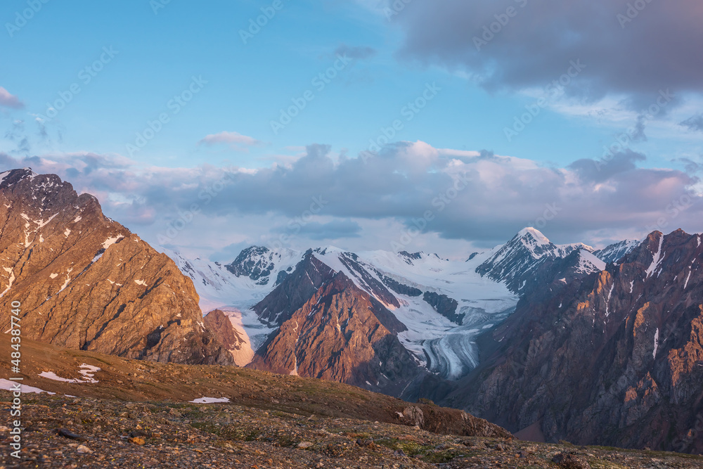 Vivid alpine landscape with high snow mountains and large glacier in sunrise colors. Colorful mountain scenery with sunlit golden rocks and mountains at sunrise. Early morning at very high altitude.
