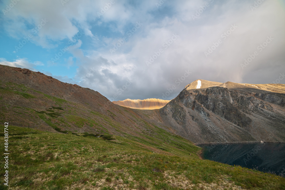 Dramatic landscape with sunlit wide sharp mountain ridge with shadows from clouds at changeable weather. Atmospheric mountain scenery with large sharp rocks on ridge top in sunlight under cloudy sky.