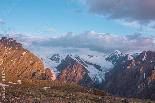 Vivid alpine landscape with high snow mountains and large glacier in sunrise colors. Colorful mountain scenery with sunlit golden rocks and mountains at sunrise. Early morning at very high altitude.