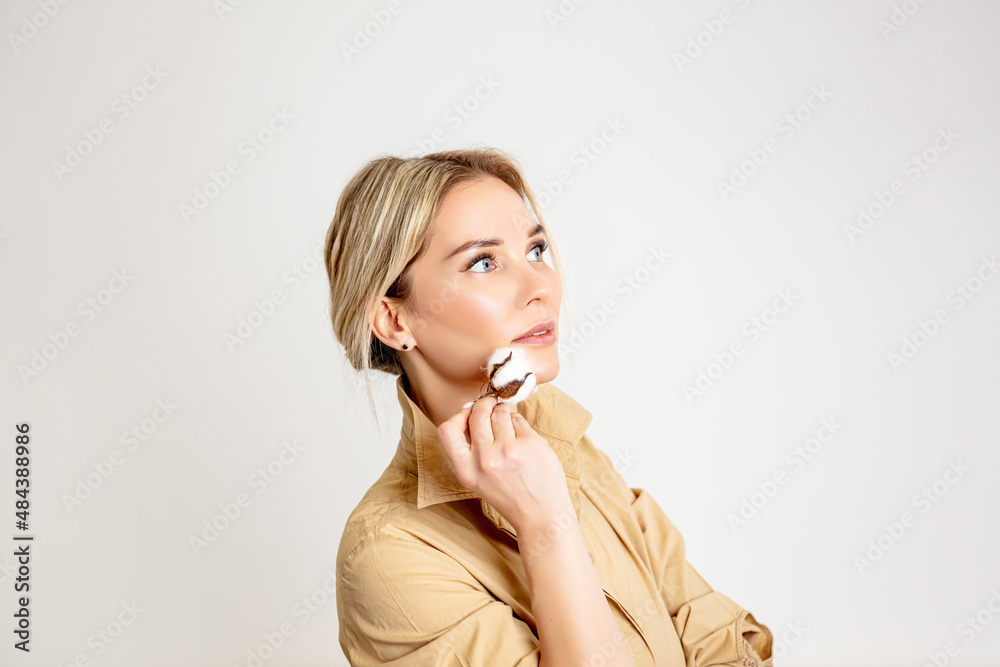 Portrait of a beautiful blonde woman with blue eyes with a branch of a cotton plant in her hand, on a light background, close-up Portrait of a beautiful blonde woman with blue eyes with a branch of a cotton plant in her hand, on a light background, close-up