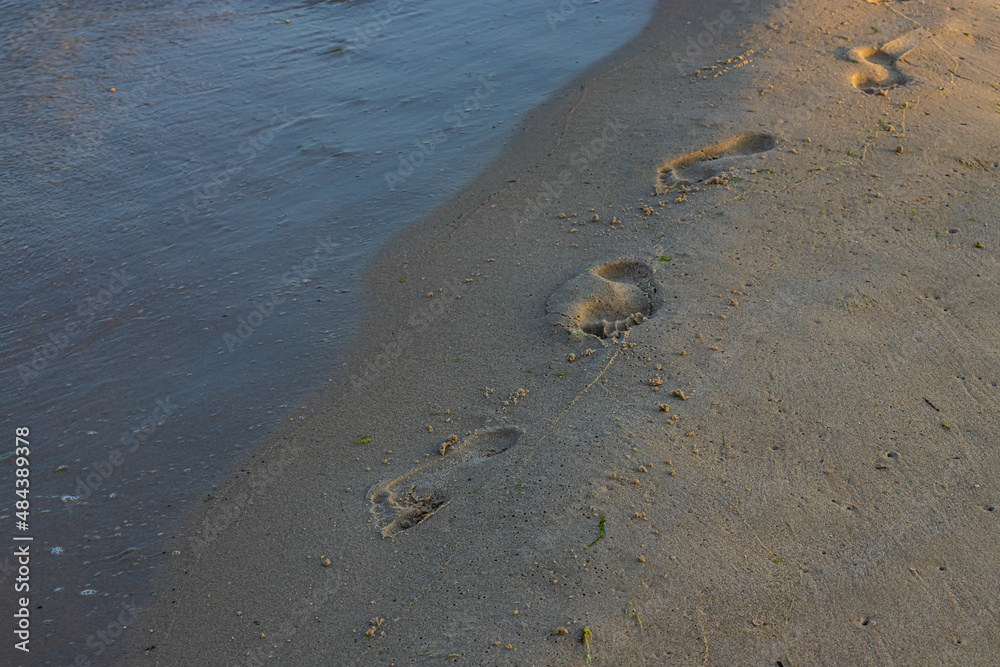 Footprints of a man on the yellow beach sand from walking barefoot by the sea with water that washes away the footprints. Footprints of a man on the yellow beach sand from walking barefoot by the sea with water that washes away the footprints.
