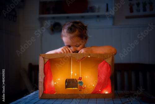 A child plays a homemade cardboard theater at home in a real interior, creative development of children, a happy childhood. photo