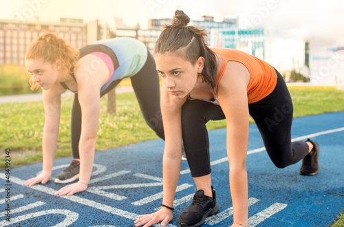 two young women on the start of a track for athletics 100 meters race, facial expression of determination and seriousness on athlete, healthy lifestyle