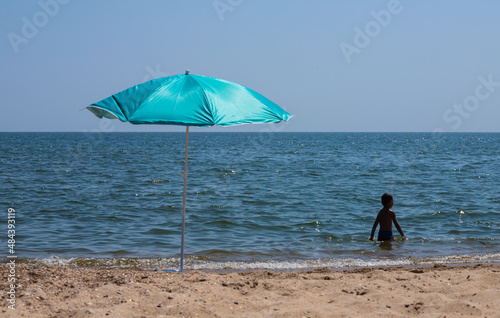 Beach umbrella with pale pink stripes in the foreground, against the blue sea background © Oleh Marchak