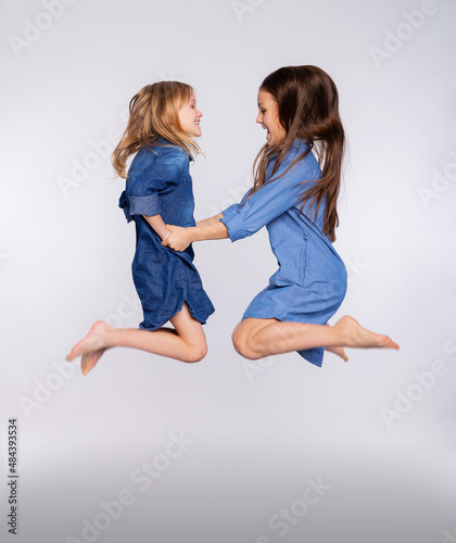 Full size portrait of two excited cute children girls enjoy jumping open mouth isolated on gray background. Loving sisters or friends jumping up playing and having fun