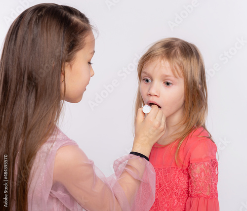Two girls friends or sister applying lipstick on lips. Helping each other doing make-up to prepare for the holiday. Together having fun isolated over white background