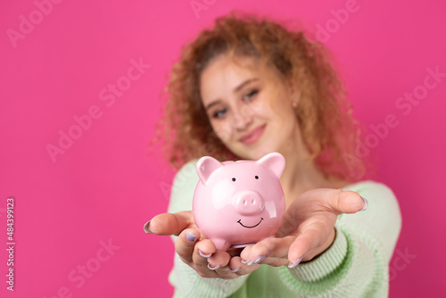 A cute young girl with curly red hair holds a piggy bank, a pink piglet in her hands. The concept of wealth and safety of money.