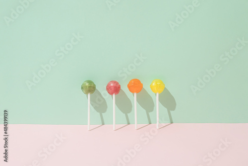 Fotografie Colorful lollipops leaning against a green wall and a pink background