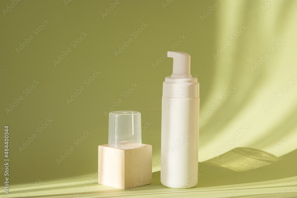 White bottle with dispenser and square stand with lid on green background, in rays of sunlight. Mock up of packaging of cosmetic lotion, cleansing foam for washing White bottle with dispenser and square stand with lid on green background, in rays of sunlight. Mock up of packaging of cosmetic lotion, cleansing foam for washing