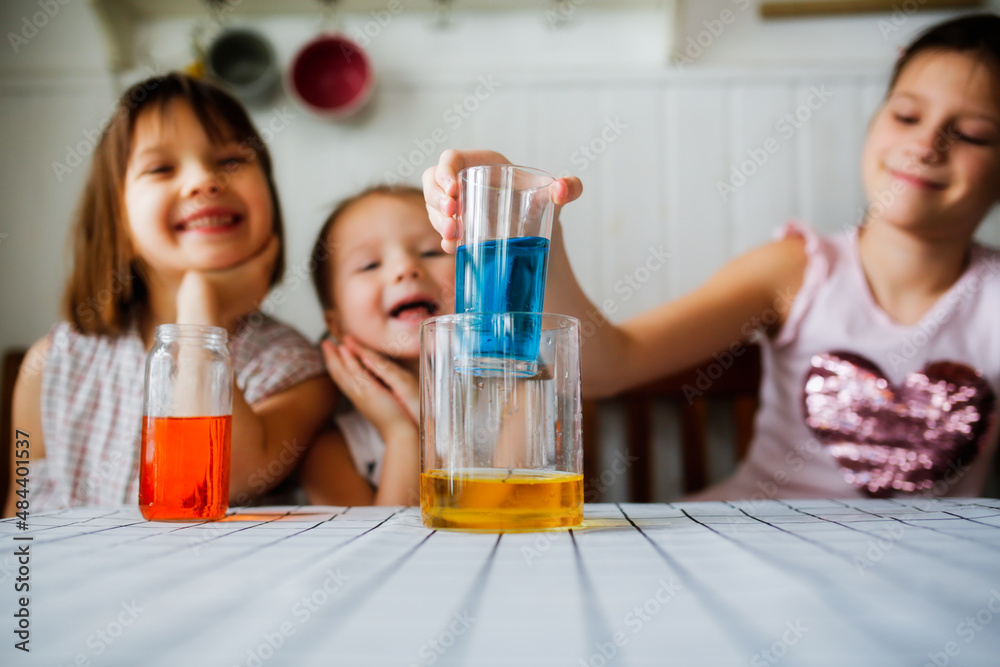 Three cute children play in the kitchen at home with colored liquids. Experiments with color at home. Three cute children play in the kitchen at home with colored liquids. Experiments with color at home.
