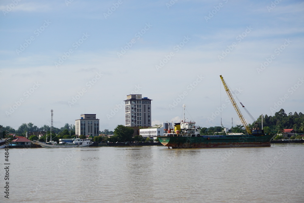 landscape photo of a loading ship with a crane on it on the Kalimantan river, and a city background, photo from far away