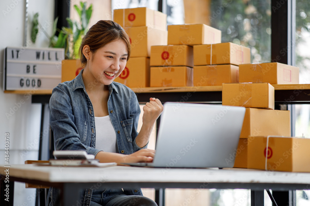 Startup SME small business entrepreneur SME or freelance Asian woman using a laptop with box, Young success Asian woman with her hand lift up, online marketing packaging box and delivery, SME concept. Startup SME small business entrepreneur SME or freelance Asian woman using a laptop with box, Young success Asian woman with her hand lift up, online marketing packaging box and delivery, SME concept.
