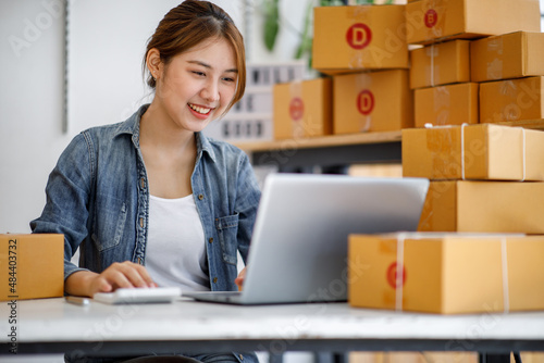 Startup SME small business entrepreneur SME or freelance Asian woman using a laptop with box, Young success Asian woman with her hand lift up, online marketing packaging box and delivery, SME concept.