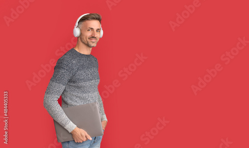 Happy man in casual listen to online audio course in headphones holding laptop, e-education photo