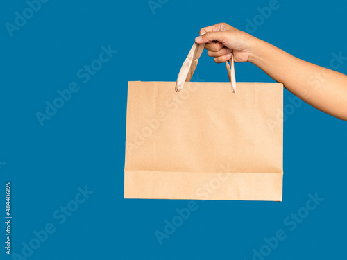 Right hand holding a brown paper bag with handle isolated on blue background. photo