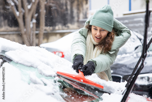 Young woman cleaning the snow from a car.
