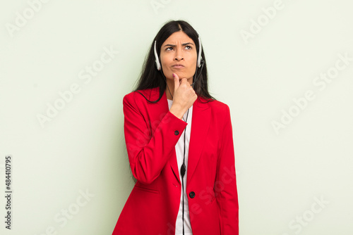 young pretty hispanic woman thinking, feeling doubtful and confused. telemarteker concpet