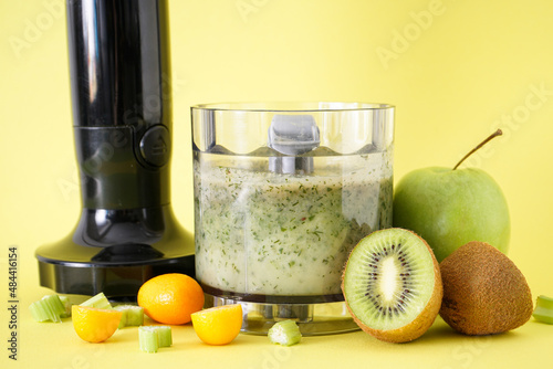 Black electric hand blender and accessories with fruits and smoothie on yellow background, close-up.