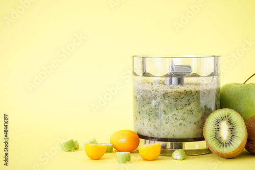 Electric hand blender with fruits and smoothie ready on yellow background, space for text.