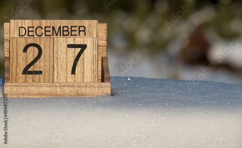 Wooden calendar of December 27 date standing in the snow in nature.