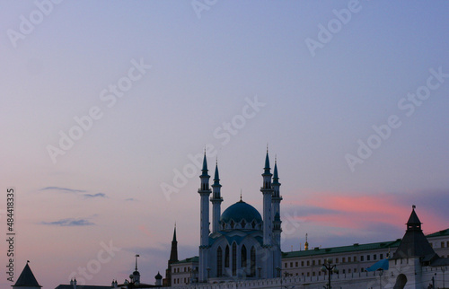 Kul Sharif Mosque in the Kazan Kremlin, Tatarstan, Russia - July 14 2021. A majestic white stone mosque with a blue roof surrounded by a red brick wall during sunset.