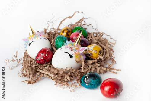 traditional Easter decoration. multicolored quail eggs and two white unicorn eggs in a nest on a white background