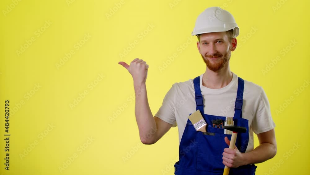 Caucasian Smiling Male Builder In Helmet Wear Blue Uniform And Pointing On Copyspace Isolated Over Yellow Background In Studio, Place For Text Or Image, Showing Empty Space For Mock Up Caucasian Smiling Male Builder In Helmet Wear Blue Uniform And Pointing On Copyspace Isolated Over Yellow Background In Studio, Place For Text Or Image, Showing Empty Space For Mock Up