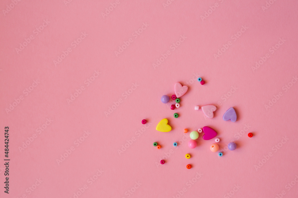 Beaded and heart-shaped beads are scattered on a pink background.