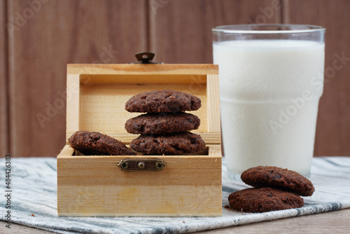 Dark chocolate cookies inside the treasury box and a glass of milk over wooden background. National cookie day