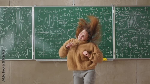 Happy female student dancing in a classroom at school against the background of a blackboard with mathematical formulas
