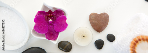 Spa setting with pink orchid, black stones and bath salts on wood background.