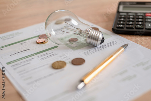 Electricity bill with light bulb, several coins, calculator and pen on the desk. Concept of electricity prices and tax payments. photo