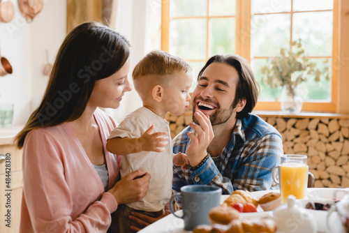 Healthy eating. Parenthood. Little small caucasian toddler infant new born baby eating berry while dad father feeding child kid. Young family of three having morning breakfast at home kitchen