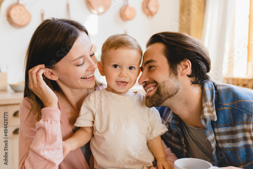 Happy family moments together. Caucasian young happy family nurturing taking care of small little kid child toddler infant baby at home kitchen. Parenthood and adoption