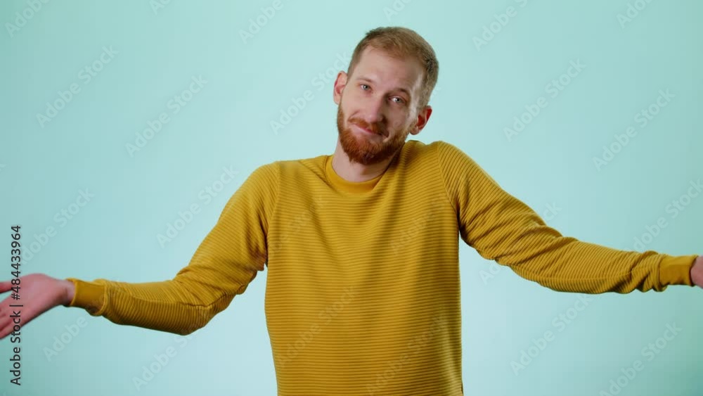 Confused Bearded Handsome Unsure Guy Looking At Camera And Shrugs His Arms, Makes Gesture Of I Don't Know, Can't Help Anything. Blue Color Background Studio. Concept Of People Emotions Lifestyle