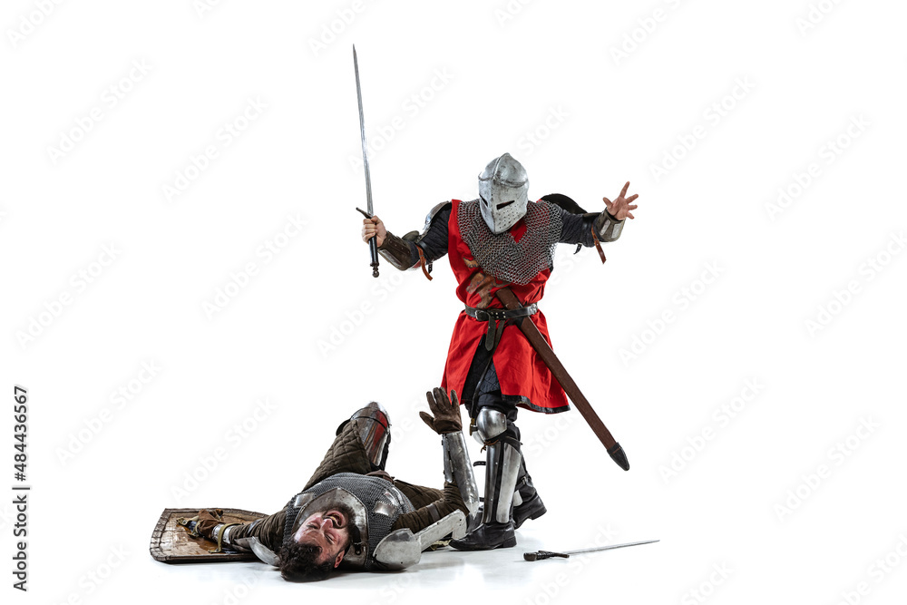 Full-length portrait of two medieval warriors, knights fighting isolated over white studio background Full-length portrait of two medieval warriors, knights fighting isolated over white studio background