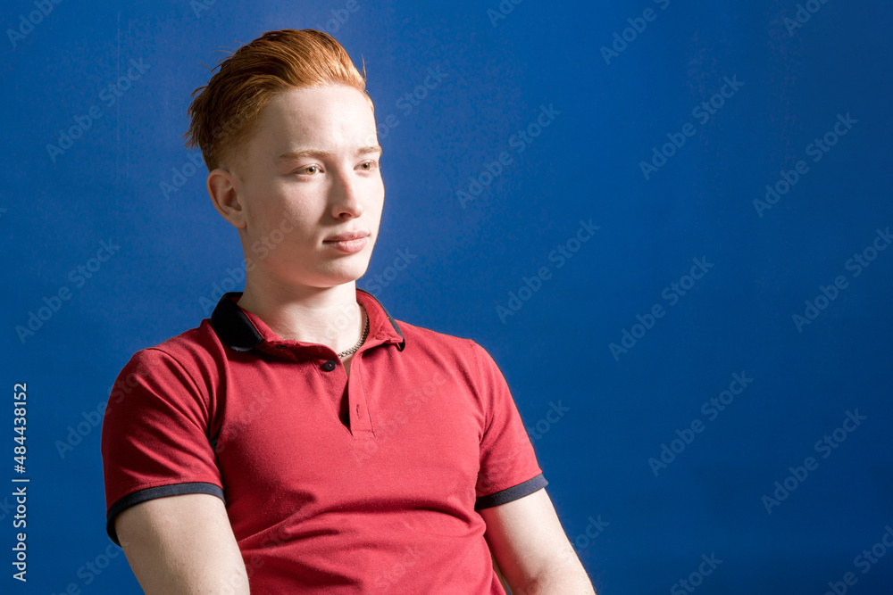 Pumped up. Coach. Sportsman. Portrait of a young red-haired athletic man, sitting in a T-shirt on a blue background. A confident, strong person. Pumped up. Coach. Sportsman. Portrait of a young red-haired athletic man, sitting in a T-shirt on a blue background. A confident, strong person.