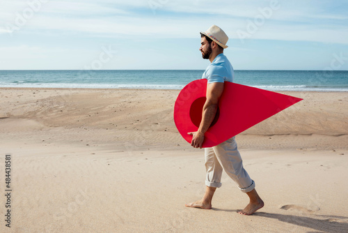 Man with red location pin walking along seashore photo