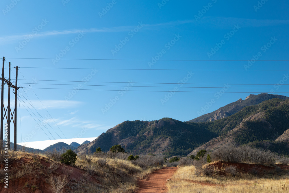 Well worn path of red dirt beneath overhead power lines, view of the Rocky Mountains beyond on a clear morning, horizontal aspect Well worn path of red dirt beneath overhead power lines, view of the Rocky Mountains beyond on a clear morning, horizontal aspect