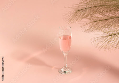 Creative idea, glass of wine with shadow and green branches of leaves. Minimal concept of drinks on pink background.