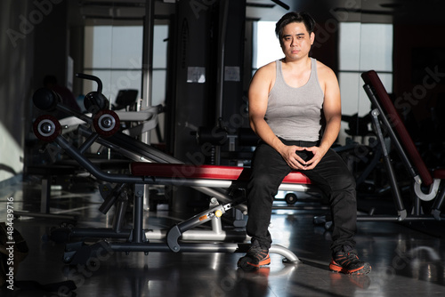 i am very boredom in this place, short hair asian man look strong wear grey tank top black plant orange snaker sitting on exercise equipment get boring during workout