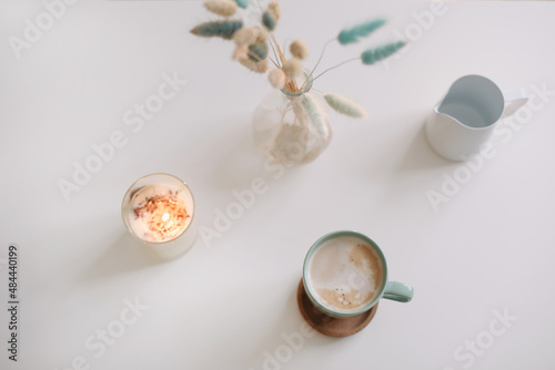 Cup of coffee and dried flowers on white background. Green mug with hot foamy cappuccino top view