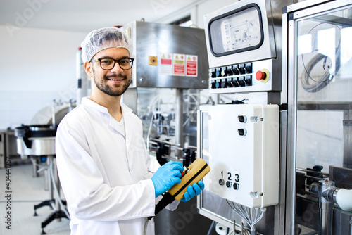 Portrait of technologist or worker in sterile white clothing standing by automated industrial machine in pharmaceutical company or factory. photo