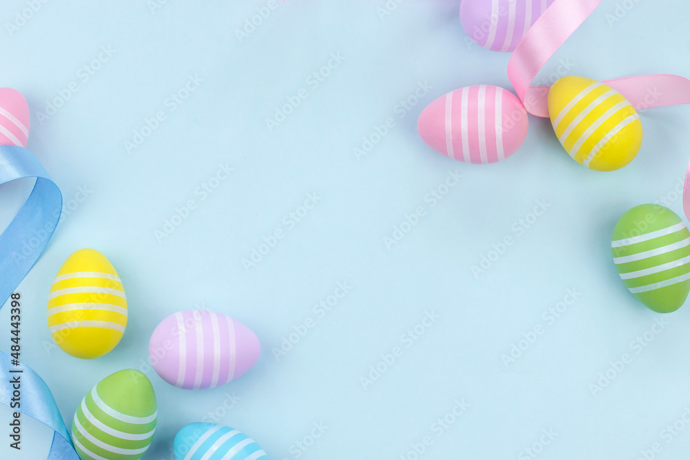 Top view of Easter eggs in pastel colors with blue and pink ribbons on light blue background. Flat lay image