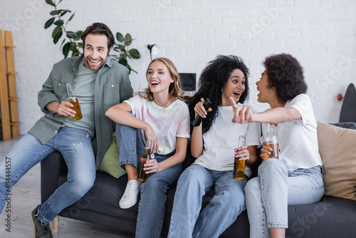 happy african american women looking at each other near friends sitting on couch and watching movie.